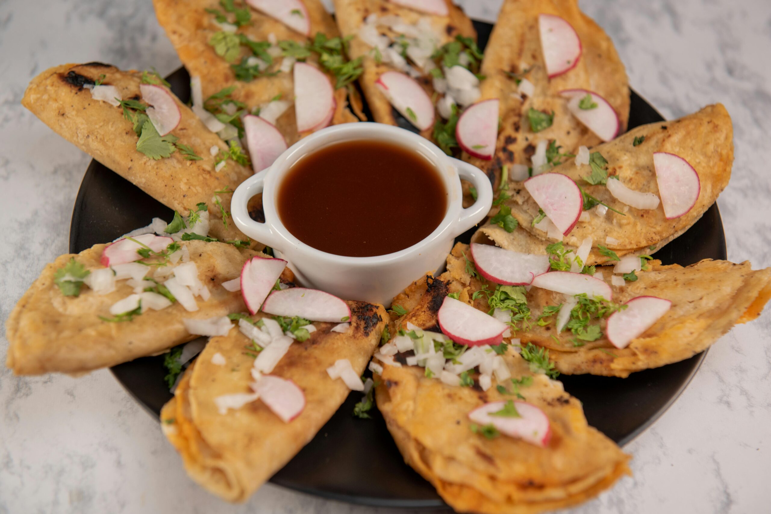 Close-up of Mexican street tacos with salsa, garnished with radish and cilantro on a marble background.